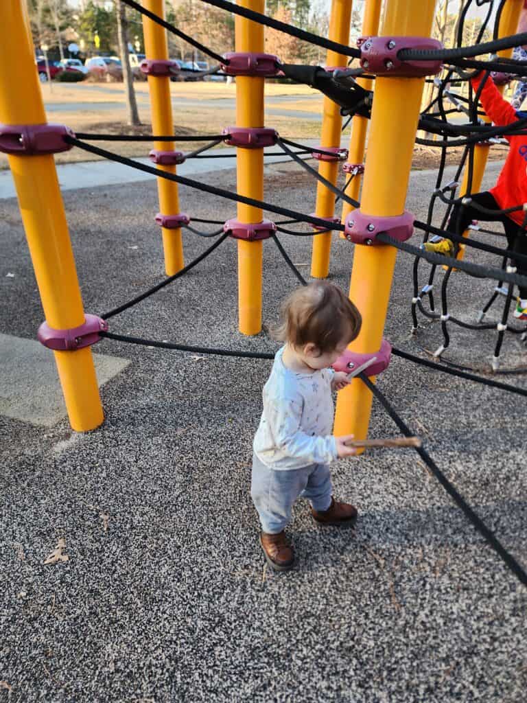 A young child explores the interactive play area at Carpenter Park Playground, engaging with the brightly colored climbing structure on a safety surface, highlighting the park's child-friendly facilities in Cary, North Carolina.