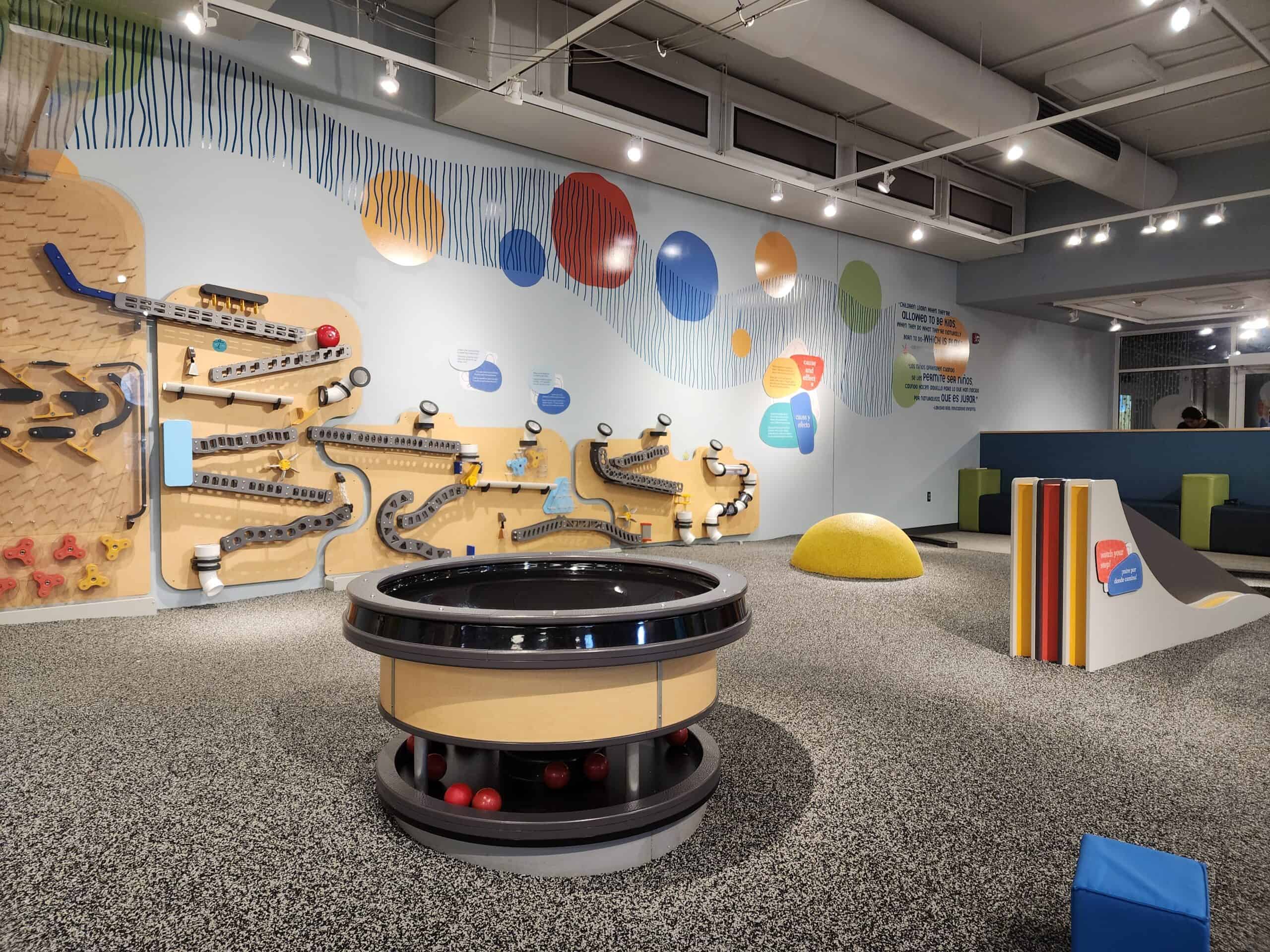 Colorful indoor playground at a facility in Durham, NC, featuring a wall-mounted ball track and interactive play areas with educational elements designed for children's creative learning and play