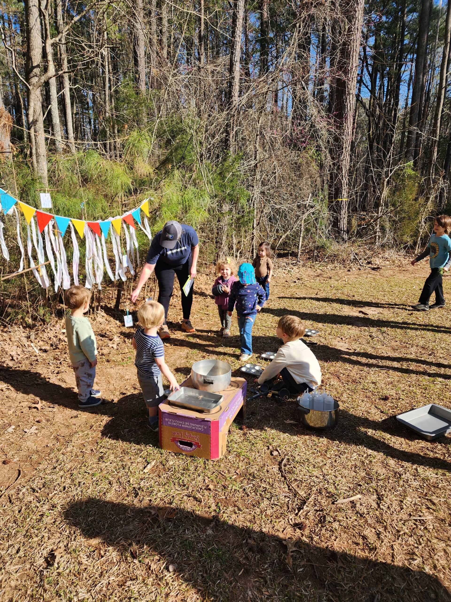 Young kids gather around an outdoor setup with pots and pans, shows a nature class for toddlers called Tinkergarten 