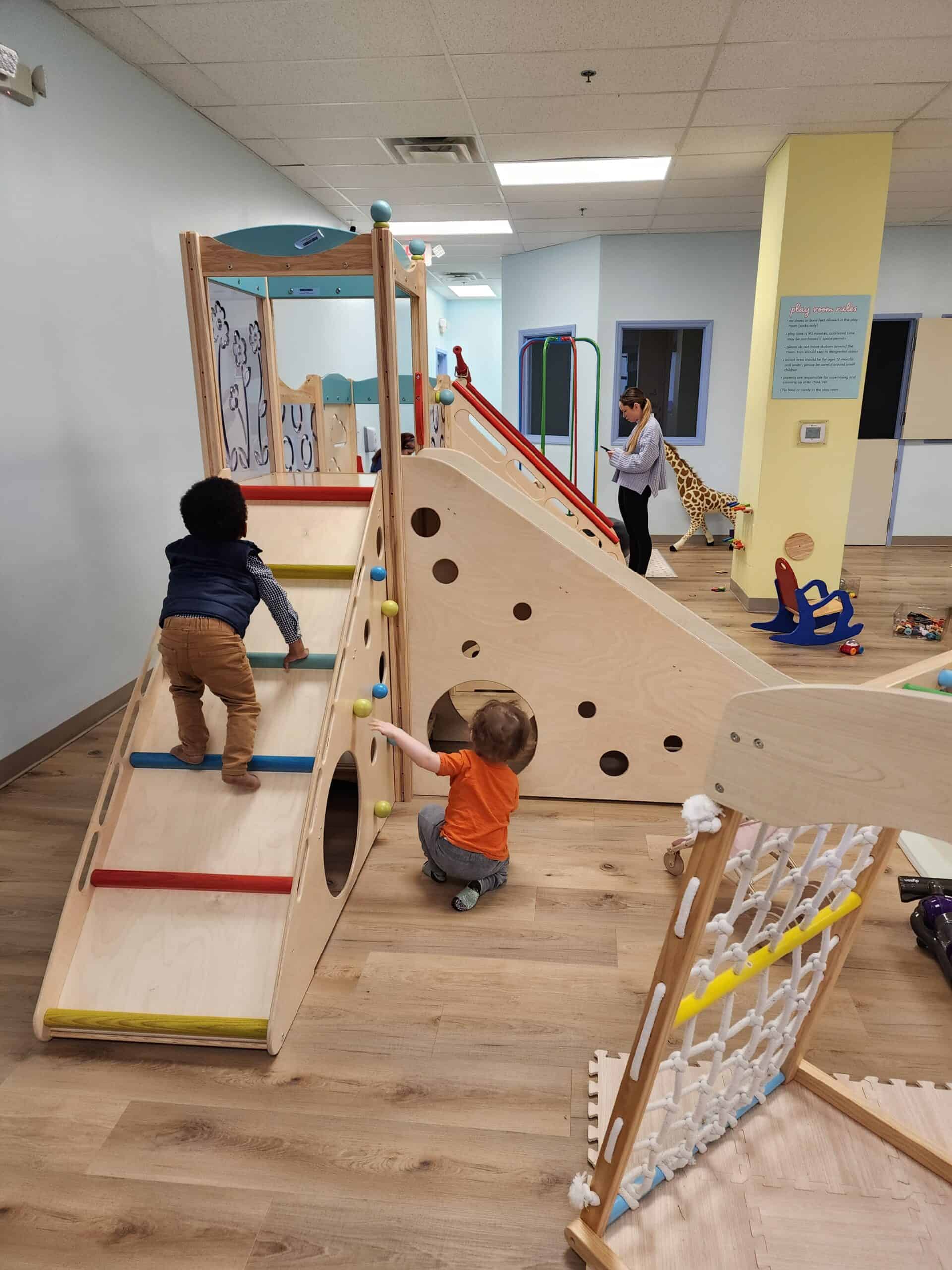 Children actively climbing and playing on a multi-level wooden play structure at Bumble Brews indoor playground in Raleigh, NC, reflecting a safe and engaging environment for kids to explore and have fun