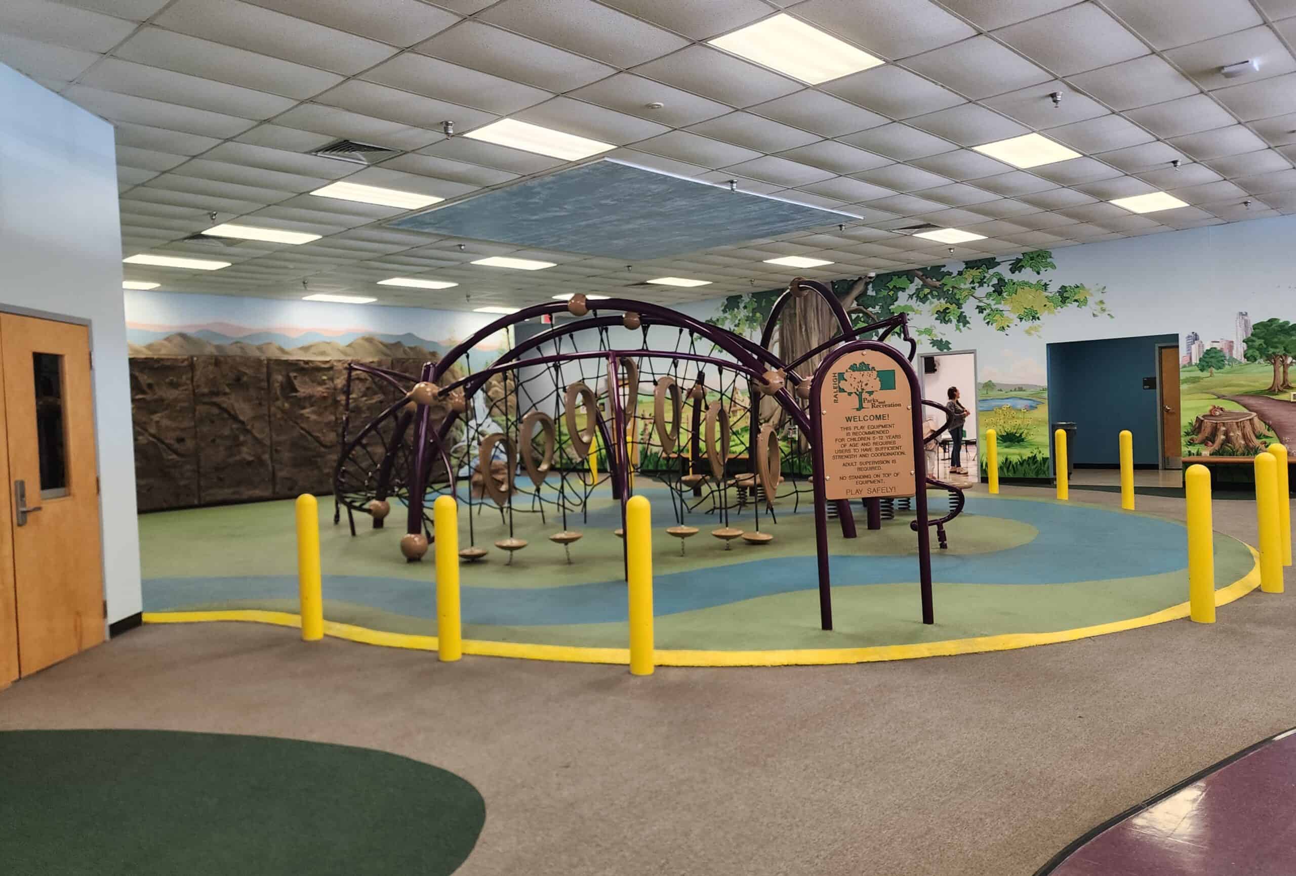 an indoor playground with lots of lcimbing structures and ropes and a nature-themed mural on the wall behind it