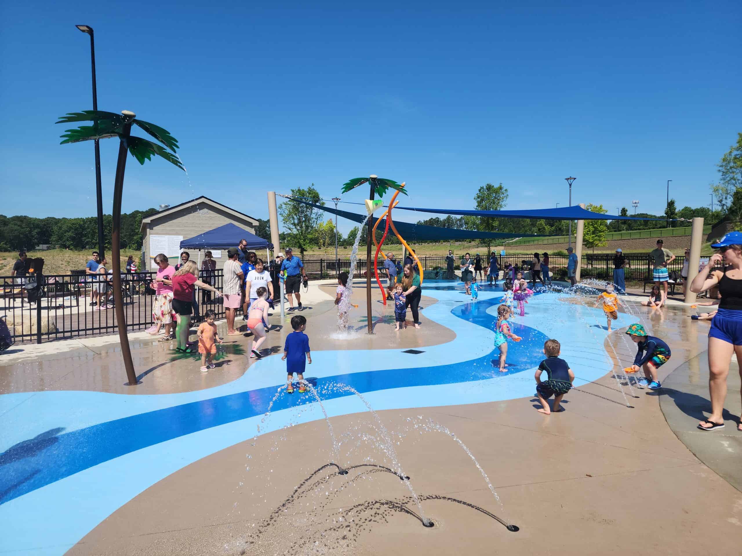 a sunny day at a splash pad in north carolina. the concrete is painted with bright blue to mimic a river