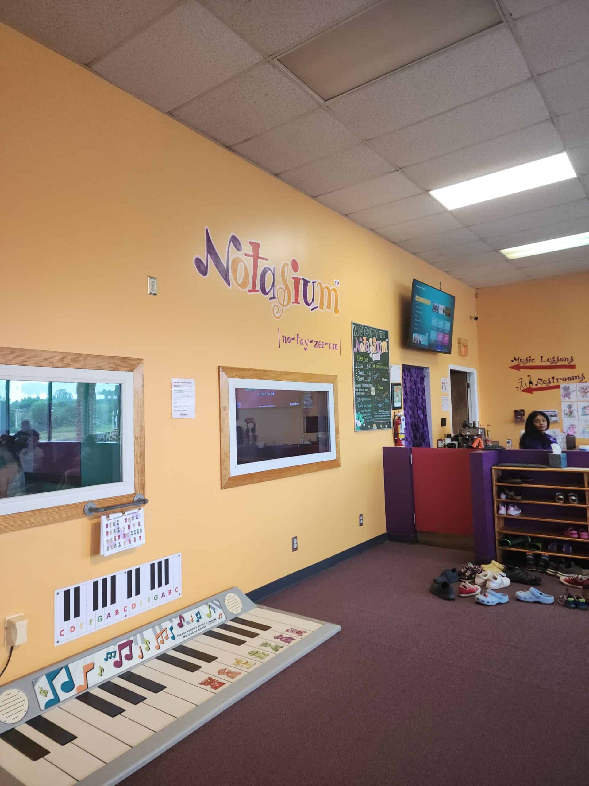 interior of Notasium play space in Durham. in the image is the name Notasium written on a yellow wall, with a floor play piano on the ground. 