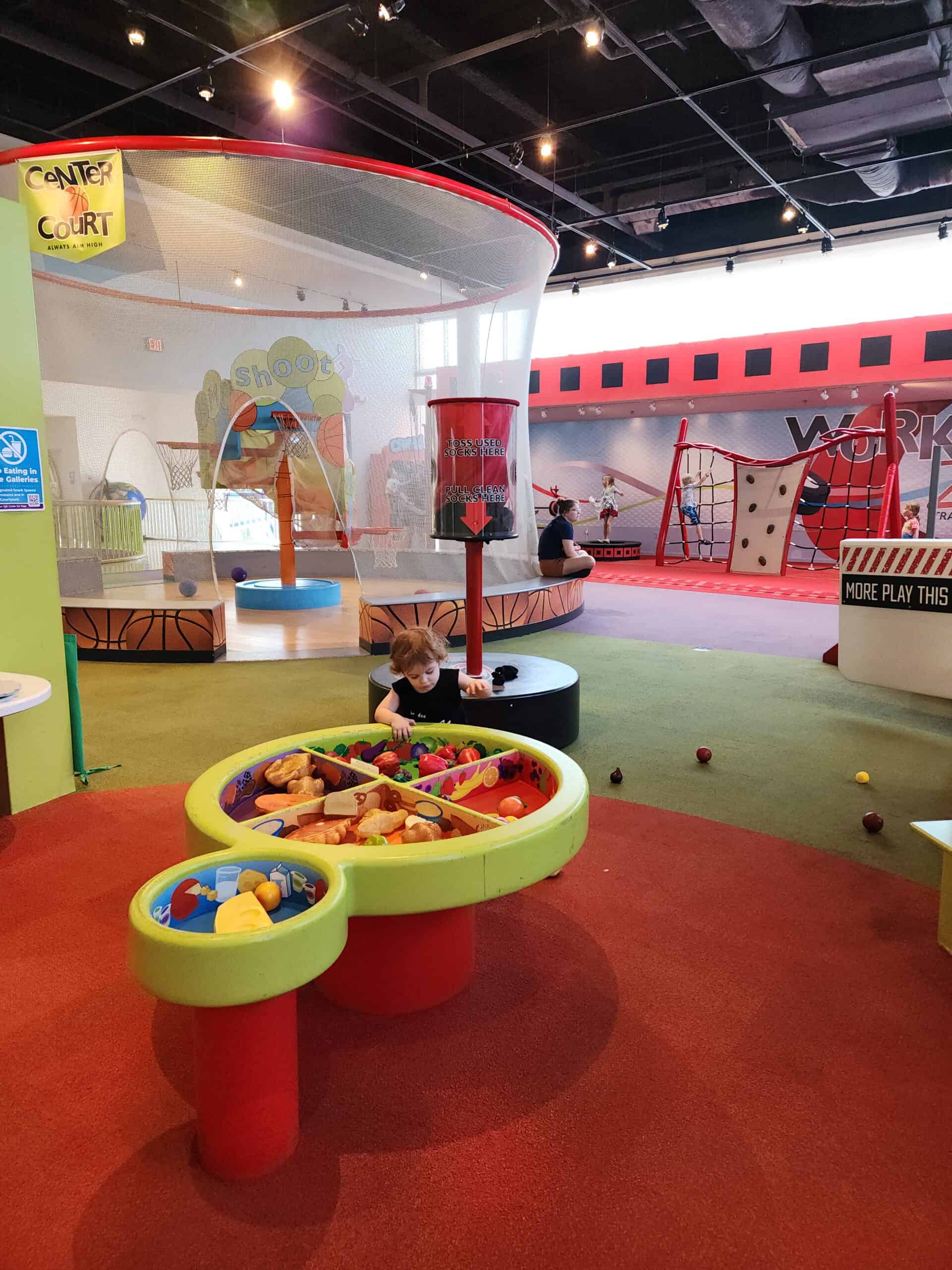 a child plays with a raised platgorm containing toy food in a colorful kids museum setting